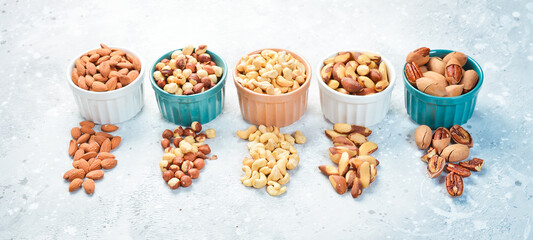 Set of nuts in bowls: almonds, hazelnuts, cashews and macadamia nuts and pecans. On a stone background.
