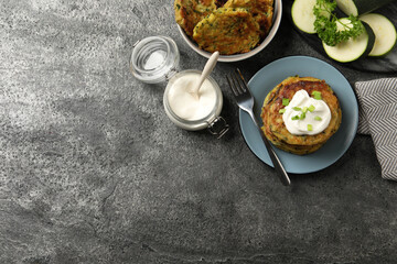 Delicious zucchini pancakes with sour cream served on grey table, flat lay. Space for text