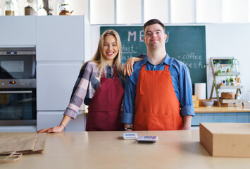 Young Down Syndrome waiter working with colleague in take away restaurant, social inclusion concept.