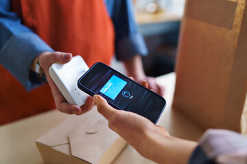 Close-up of waiter taking contactless smartphone payment from costumer in take away restaurant.