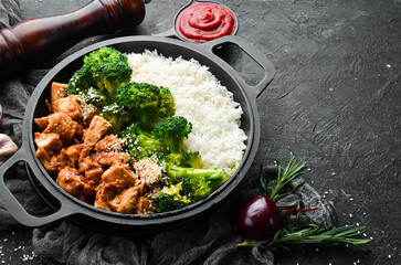 Healthy food. Chicken with teriyaki sauce, boiled rice and broccoli in a black pan. Rustic style. Top view.