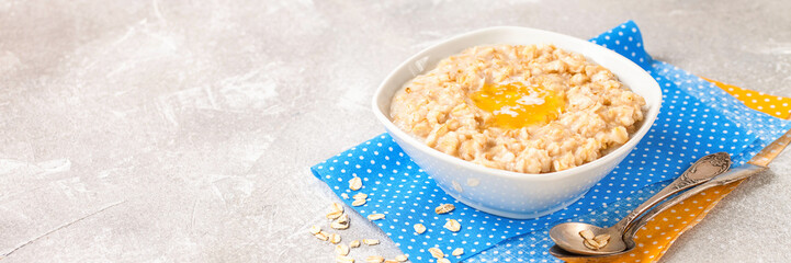 Porridge with oil in a bowl on a gray concrete background. Healthy useful breakfast. Selective focus. Copy space