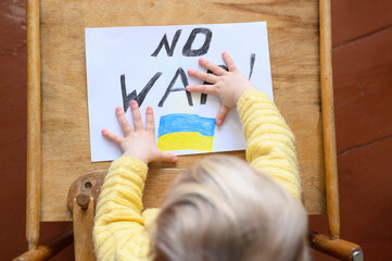 Ukrainian girl kid protesting against war conflict and drawing message text No War with Ukrainian flag on the white paper. No war, stop war, russian aggression, crisis, peace, stop aggression