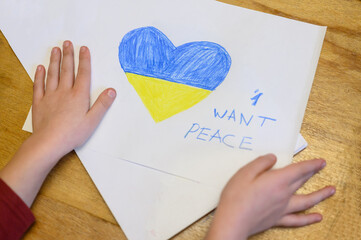 Ukrainian girl kid hands protesting against war conflict and holding a white paper with message text "I want peace". Painted heart with Ukrainian colours flag. No war, stop war, russian aggression, , 