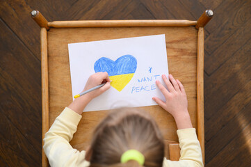 Ukrainian girl kid protesting against war conflict and holding a white paper with message text "I want peace". Painted heart with Ukrainian colours flag. No war, stop war, russian aggression, crisis, 