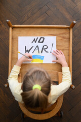 Ukrainian girl kid protesting against war conflict and drawing message text No War with Ukrainian flag on the white paper. No war, stop war, russian aggression, crisis, peace, stop aggression