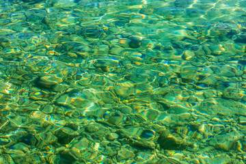 Water background abstract, calm transparent water waves, trendy abstract nature background. Sunlight. Blurred of sea green water surface which has stone background below.