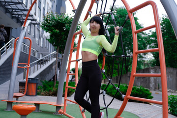 woman in sportswear doing sport exercises outside on modern sport trendy playground. healthy slim body. modern new buildings background.