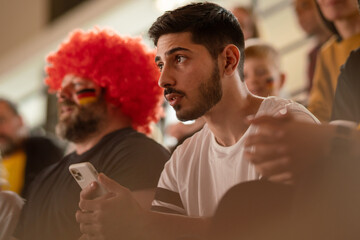 Worried football fans supproting German national team in live soccer match at stadium.