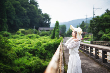 Fototapeta na wymiar 田舎の古い橋の上に佇む白いワンピースと帽子の若い日本人女性