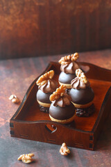 Chocolate Profiteroles (Cream Puffs) dipped in chocolate, garnished with whipped chocolate cream and walnuts, on a chocolate crunchy cookie base, on a dark brown background. 