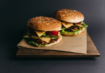 Delicious big juicy burger with tomatoes, cucumbers, cabbage, greens, cheese, cutlet on a gray background. Two sandwiches, fast food. Snack, appetizing, bun with sesame seeds. Serving in restaurant