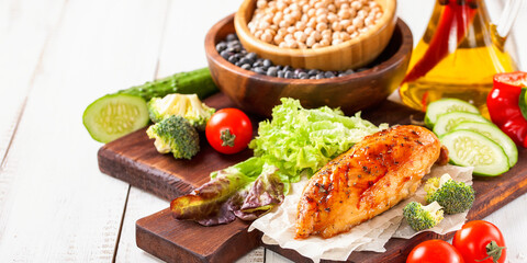 The baked chicken fillet and vegetables. Healthy and fitness food. Meat, salad, vegetables, nuts, beans on a light wooden background. Selective focus. Copy space