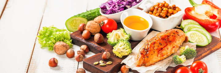 The baked chicken fillet and vegetables. Healthy and fitness food. Meat, salad, vegetables, nuts, beans on a light wooden background. Selective focus. Copy space