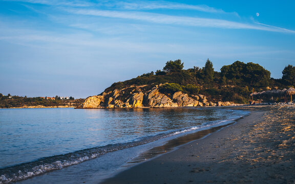 View of the coast beach in the background a rocky ledge covered with green trees and bushes. Ormos Panagias, Greece