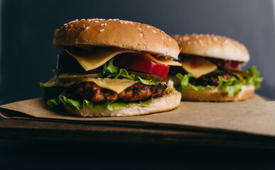 Delicious big juicy burger with tomatoes, cucumbers, cabbage, greens, cheese, cutlet on a gray background. Two sandwiches, fast food. Snack, appetizing, bun with sesame seeds. Serving in restaurant