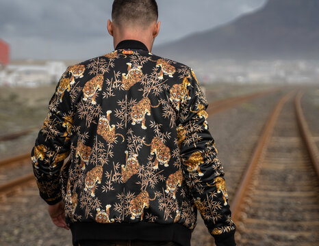 Rear view of a young male in a tiger print jacket walking on the railroad tracks