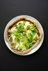 Homemade pizza on a white plate, with dark background, copy space