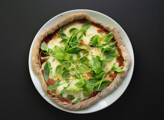 Homemade pizza on a white plate, with dark background, copy space