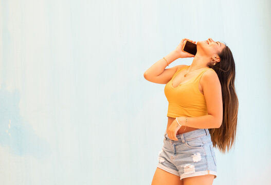 Mujer joven con tel&eacute;fono m&oacute;vil aislado sobre fondo gris con sorpresa y expresi&oacute;n facial conmocionada,short corto,pantalon corto,top,celular,