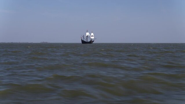Old VOC vlieboot with bulging white sails in open sea; aerial long shot