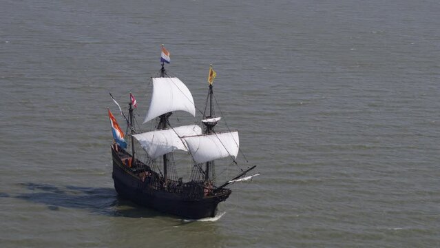 Replica of historic VOC ship sailing in open seas, Dutch flags flutter; drone