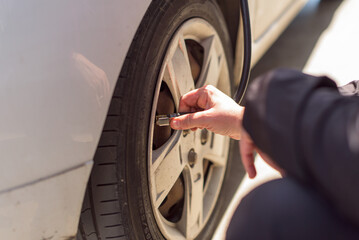 A woman's hands place the air hose on the car wheel to flatten the car tires.