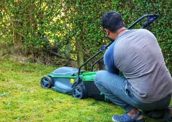 Fototapeta premium An unrecognizable asian indian man sitting on grass and adjusting the grass basket from a electric lawn mower machine.