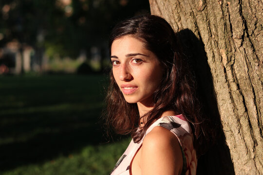 Beautiful Middle Eastern woman wearing a dress leaning a tree in the park