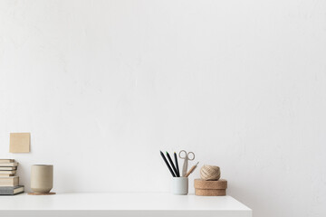 Empty space at office table. Mug, books, boxes, pencils on white desk with white wall copy space.