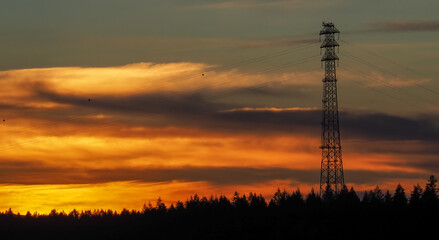 Fototapeta premium Dramatic sunset behind a very tall transmission tower and its associated power lines.