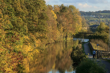 Autumn colours reflected in the Leeds and Liverpool Canal near Bingley with the towpath inviting walkers and hikers to enjoy a relaxing peaceful time close to nature