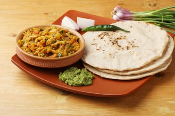 indian village food roasted egg plant and bhakri or Indian flat bread  Jowar Roti served with green chilli chutney traditionally called as Theccha in Marathi and spring onion beside 
