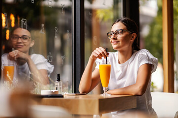 A happy college girl sitting in the cafeteria at her break and having fresh orange juice.