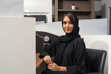 Portrait of a cheerful Arabian businesswoman sitting at the table in office and looking at camera