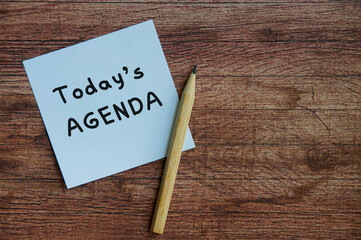 Today's agenda on white notepad with wooden table background.