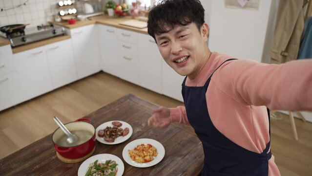 mobile cam view of happy asian dad showing delicious dish he made to family through video chat online call. he looks at camera while smelling food and boasting about his cooking