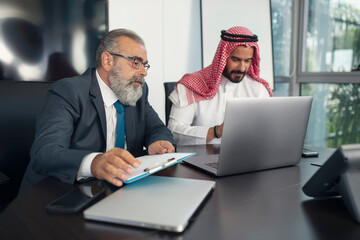 Business meeting in the office, Arabian businessman having a business conversation with a Mature businessman and working on the laptop 