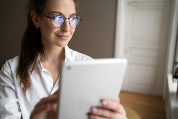 Uses a tablet a woman with glasses looks at the camera in a white shirt sitting in the office