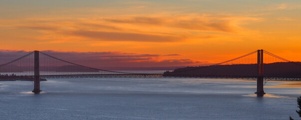 The Tacoma Narrows Bridges tower over Puget Sound with Fox Island in the distance during a dramatic sunset.