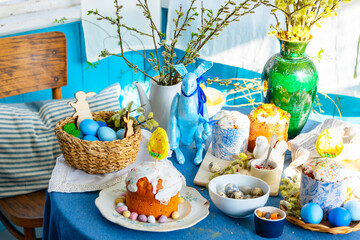 table set for Easter on veranda on sunny spring day decorated with flowers and Easter decor, eggs, cake and willow branches, Easter family celebration