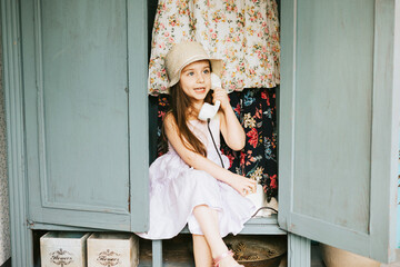 little cute Armenian girl sit in retro vintage wardrobe and playing hide-and-seek in country house...