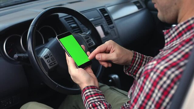 Millennial man driver holding smartphone in his hands closeup, using app on mobile phone in hos hands with chroma key in car