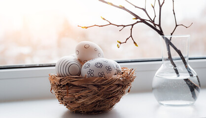 Easter composition. Willow branches in a vase, painted eggs in a nest on the windowsill by a wet...