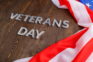 the words veterans day laid with silver metal letters on wooden board surface with crumpled usa...
