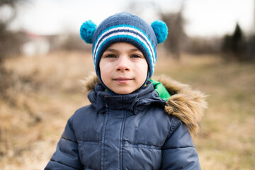 Portrait of little adorable boy in warm clothes against rural background in spring