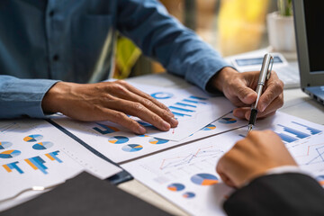 Two businessmen sit down to analyze financial data from earnings graphs showing the company's earnings to be presented at a meeting.