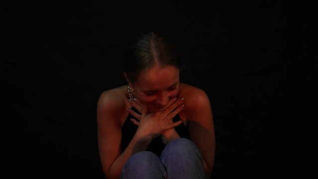 Happy, smiling and happy teenage girl sitting down in front of a black background