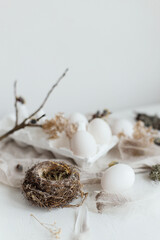 Easter simple aesthetics. Easter natural eggs, feathers, willow branches, nest on rustic white table. Stylish rural Easter still life in pastel white and beige colors.