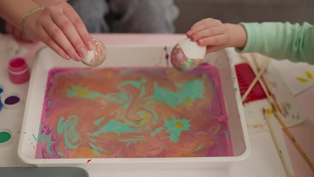 Lady with little child colors eggs with marbling art method
